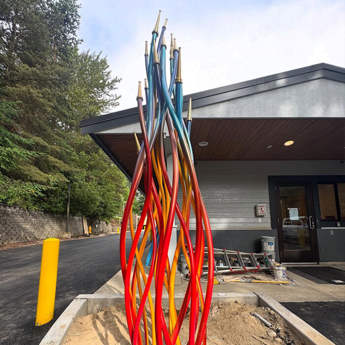 Public art metal sculpture "Unity Flame" at Kirkland Fire Station 21, fabricated by Engineered Artworks for artist Sean Orlando, featuring curving steel tubes and fire nozzle details.